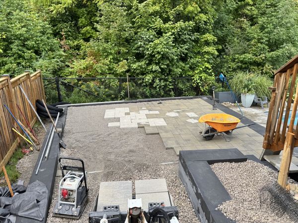 Interlocking stone patio being laid beside a new retaining wall.